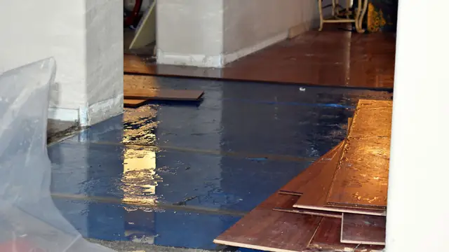 Wet subfloor under lifted wood style planks with plastic sheeting along the wall
