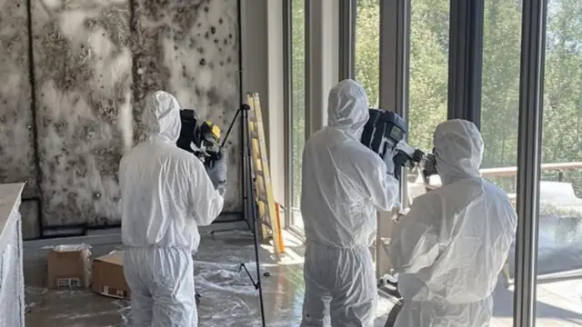 Team in protective suits carrying out an inspection with camera equipment in a room with mold on the wall