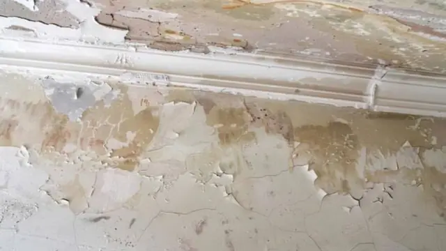 Wall with peeling paint and water stains above a baseboard