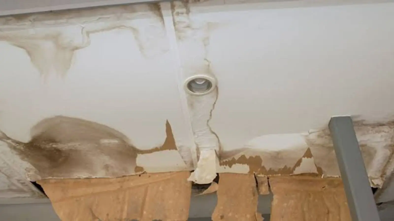 Water stained ceiling with peeling material around a pipe fitting