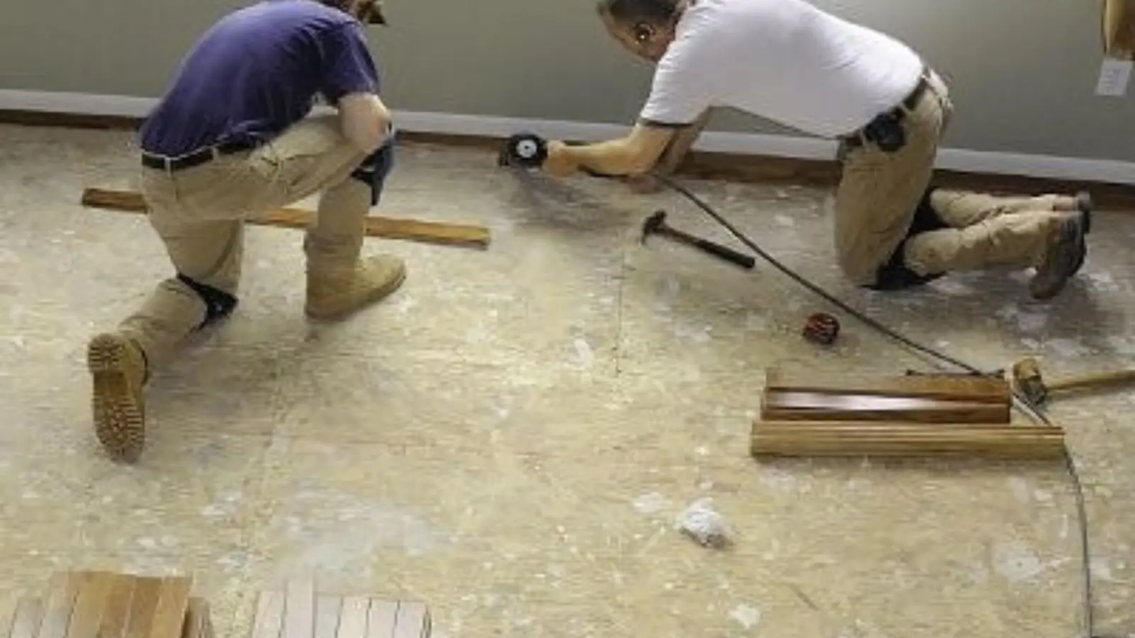 Two technicians kneeling on a subfloor measuring and fitting new flooring during water damage repair